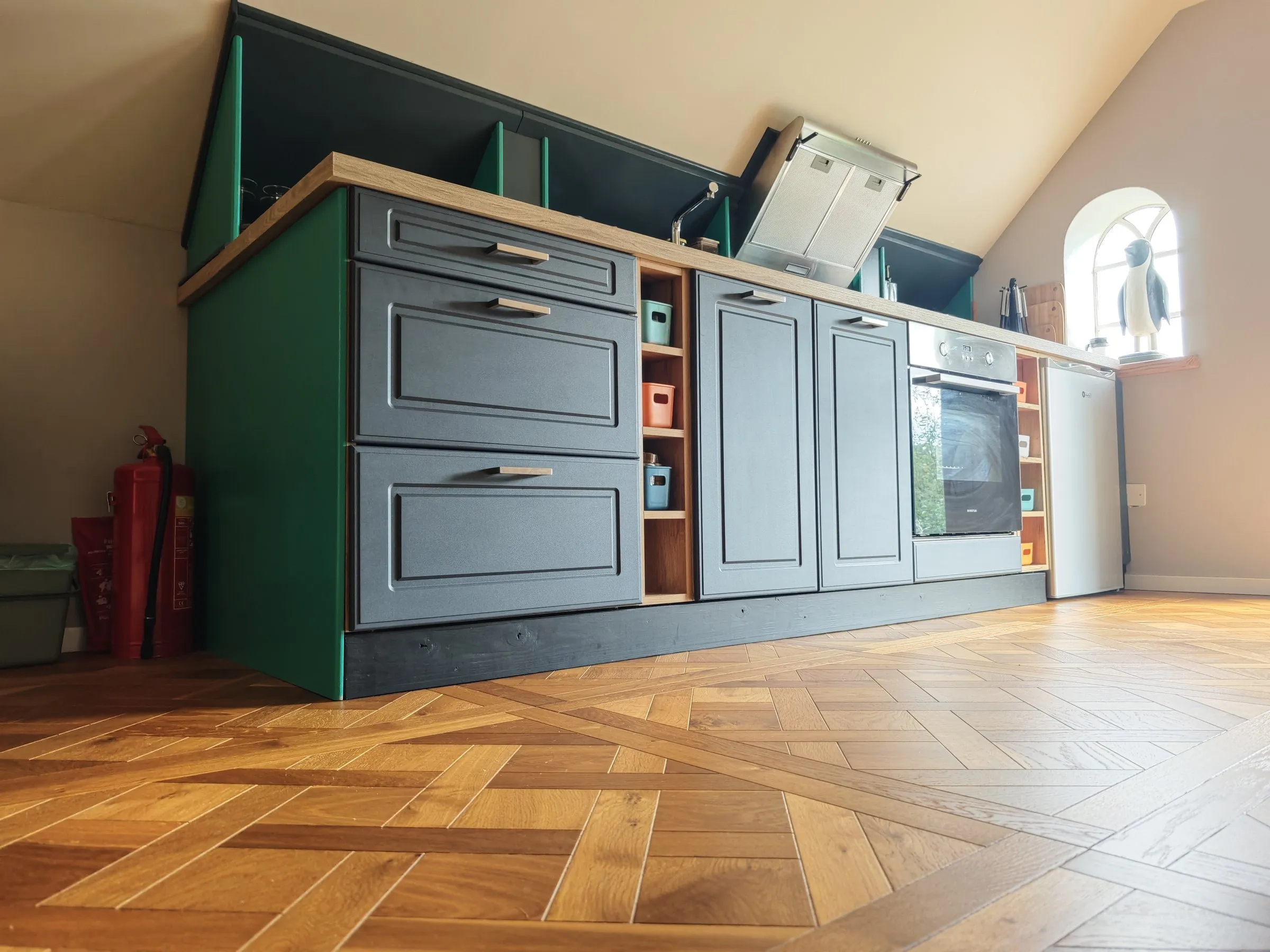 Keuken met groene kasten, houten werkblad en visgraatvloer