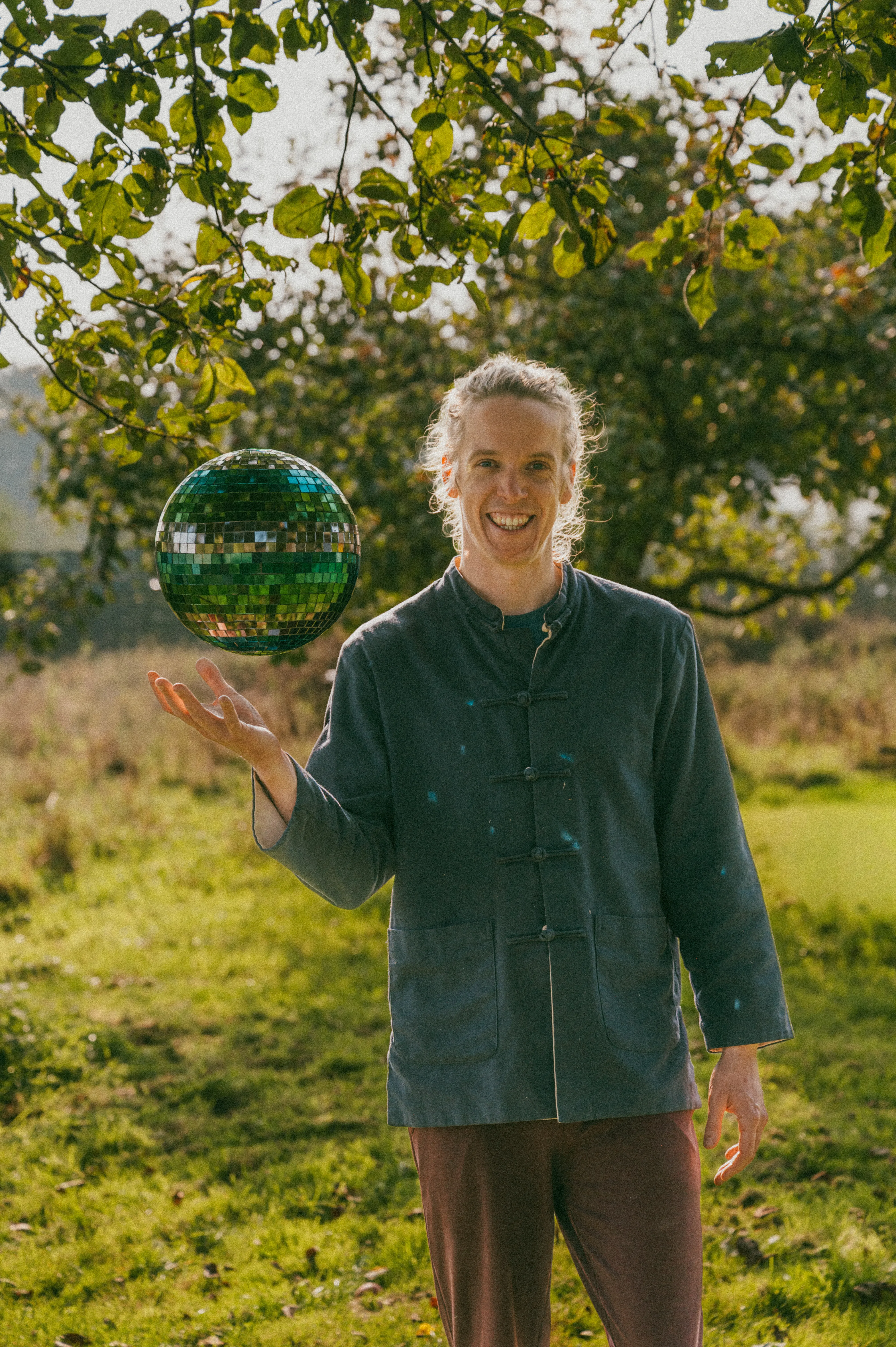 Noud lachend in een boomgaard, met een discobal boven zijn hand